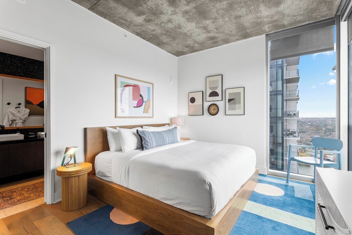 Une chambre moderne avec un grand lit, une vue sur la ville et un balcon équipé d’une chaise.