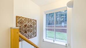 Een trap met een houten leuning, een wandpaneel ter decoratie, en een raam met uitzicht op een bakstenen muur en bomen.