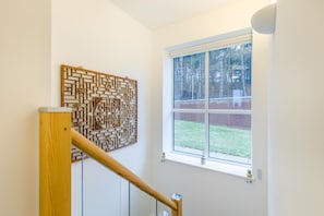 A staircase with a wooden handrail, a wall-mounted decorative panel, and a window with a view of a brick wall and trees. - 2 Bed in Upper Sheringham (oc-a34684) (Upper Sheringham)