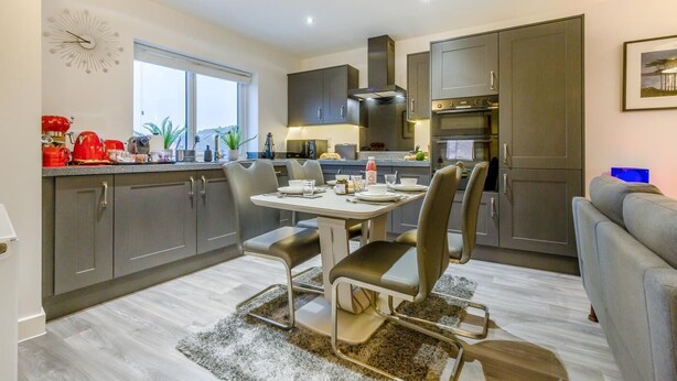 Een moderne keuken met donkere kastjes, een eettafel met stoelen en een groot raam.