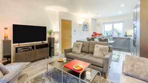 Een moderne woonkamer met een flatscreen televisie, bank, salontafel en een eethoek, met een keuken op de achtergrond.