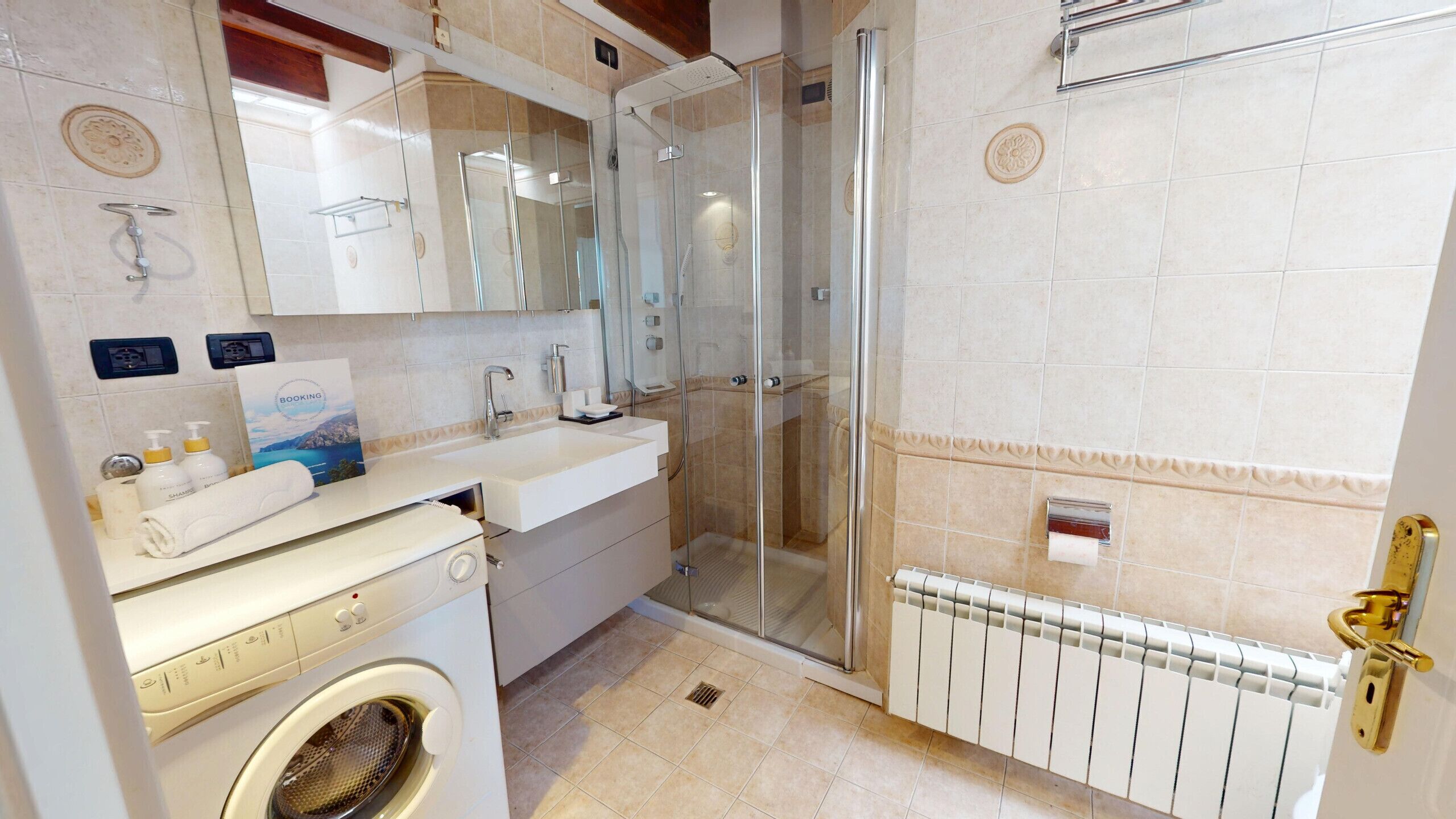 A bathroom with a glass shower enclosure, a built-in washing machine, and a radiator.