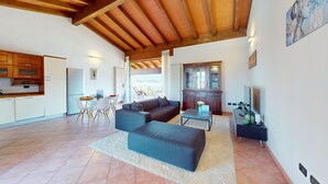 A spacious living area with a wooden ceiling, a dining table with chairs, a sofa, a TV, and a kitchen area with cabinets. - Lido Apartment by Booking Lake Garda (Manerba del Garda)