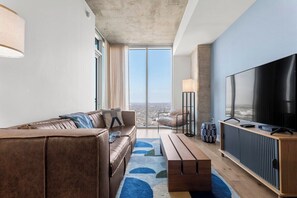 A modern living room with a leather sofa, a wooden coffee table, a TV, and a large window with a city view. - 3006 ATX Cozy Prestige Condo | Rooftop Pool & Firepit, Rainey St Nightlife (Austin)