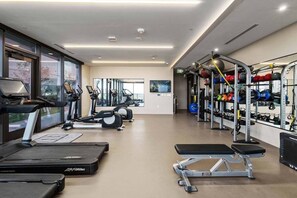 Ein Fitnessstudio mit Laufbändern, Crosstrainern, einer Hantelbank und Gewichten.