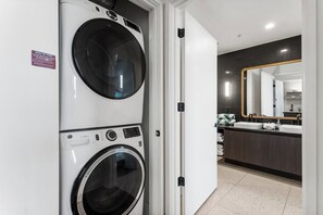A laundry area with stacked washers and dryers, a bathroom with a large mirror and modern fixtures. - 3006 ATX Cozy Prestige Condo | Rooftop Pool & Firepit, Rainey St Nightlife (Austin)