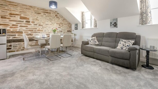 A loft-style room with a stone wall, a grey sofa, a dining table with chairs, and a small round table with cups.