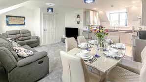 A modern living room with a sofa, a dining table set for four, and a kitchen area with a window.