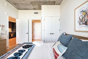 A bedroom with a bed, pillows, a blanket, a wardrobe, and a door leading to a bathroom. - 2906 ATX Sunrise Chic | Rooftop Pool, City Views & Rainey St Nightlife (Austin)
