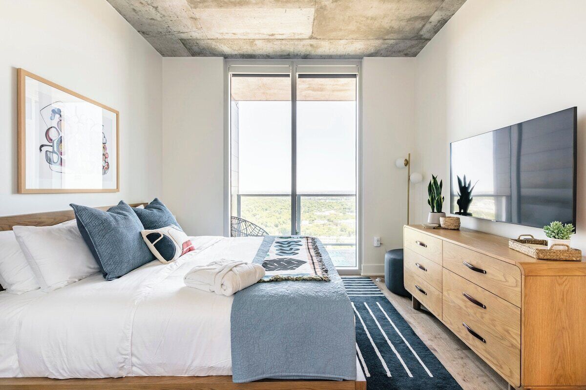 A bedroom with a bed, a large window, a TV, and a wooden dresser.