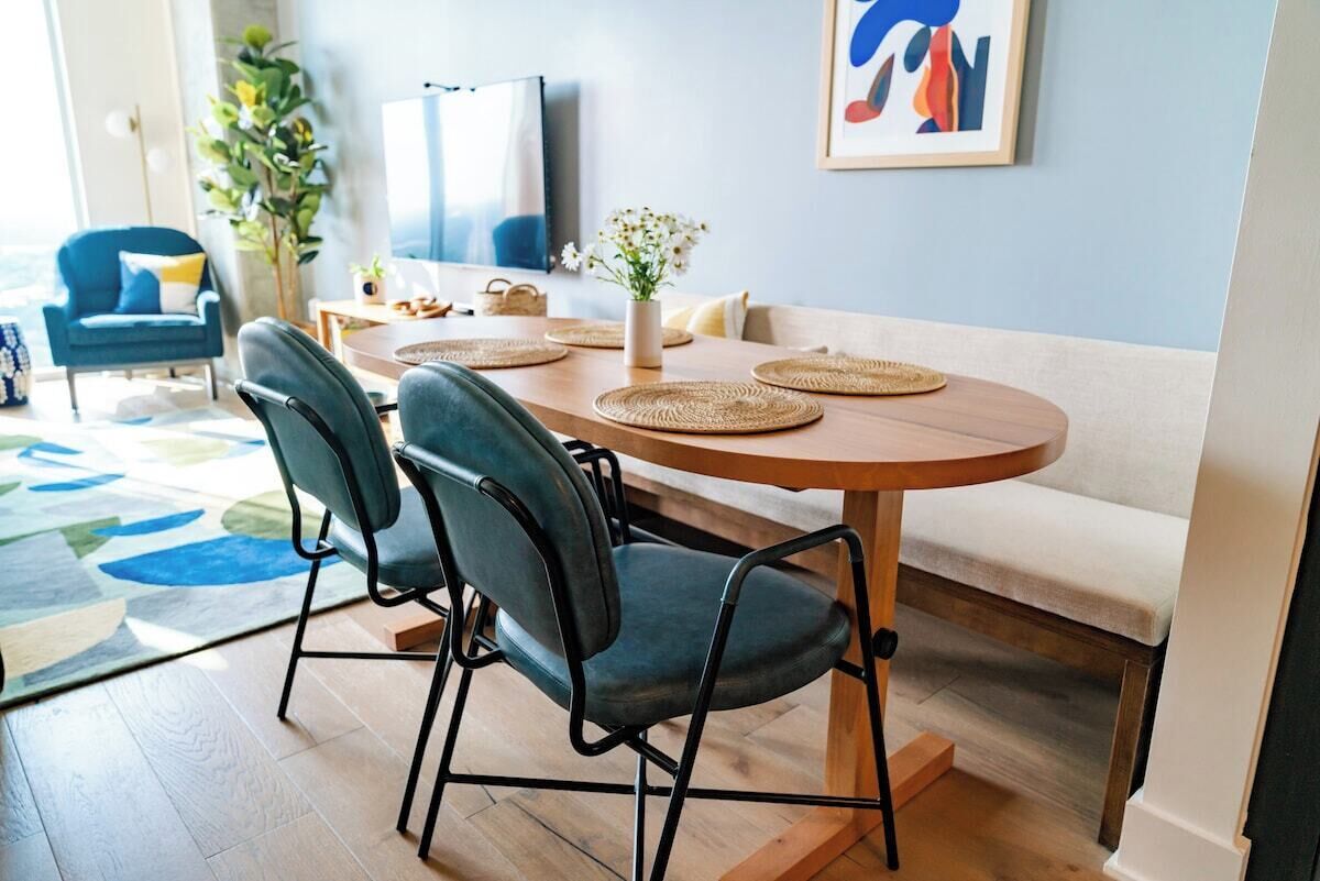 A dining area with a round table, four chairs, a vase with flowers, and a painting on the wall.