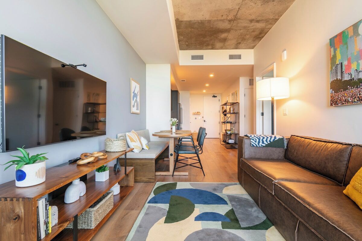 A modern living room with a sofa, a coffee table, a TV, and a dining area with chairs and a table.