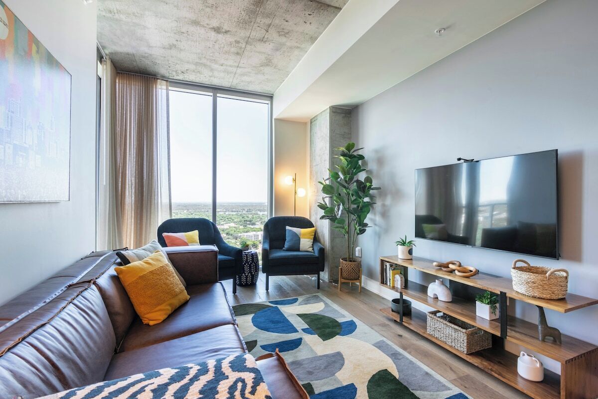 A modern living room with a large window, a sofa, a chair, a TV, and a plant.