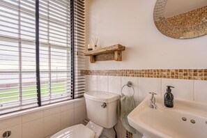 Une salle de bain avec des toilettes, un lavabo et une fenêtre avec des stores.