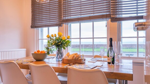 A dining area with a table set for four, a vase with yellow flowers, a bowl of oranges, and a bottle of wine. - 3 Bed in Dysart (oc-p34376) (Dysart)