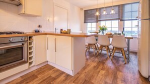 A modern kitchen with a built-in oven, a dining area with a table and chairs, and a view through large windows. - 3 Bed in Dysart (oc-p34376) (Dysart)