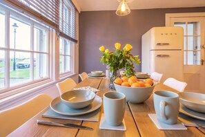 Un coin repas avec une table dressée pour quatre personnes, un vase rempli de fleurs jaunes et un réfrigérateur blanc.