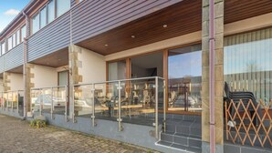Ein modernes Gebäude mit überdachtem Außenbereich, großen Fenstern und einem gepflasterten Eingang.