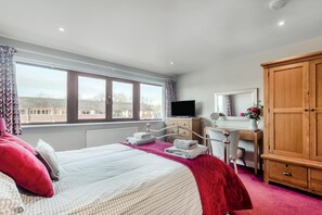 Ein Hotelzimmer mit Bett, Schreibtisch, Fernseher, Kleiderschrank und Fenster mit Blick auf Gebäude.