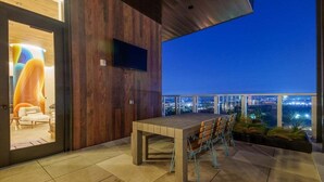 A modern outdoor dining area with a wooden table and chairs, a flat-screen TV mounted on the wall, and a city view at dusk. - Modern Luxury Downtown, Mins to Everything (Austin)