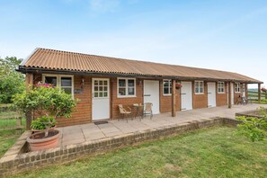 Ein Holzhaus mit Ziegeldach, einer gepflasterten Terrasse und einem kleinen Garten mit Blumentöpfen.