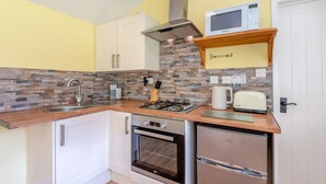 Uma cozinha compacta com armários brancos, fogão a gás, micro-ondas e forno embutido.