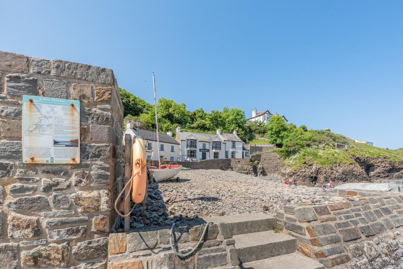 A stone wall with a sign, a boat, and a building with a white facade.