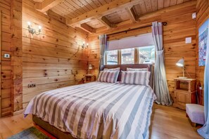A wooden cabin bedroom with a bed, bedside lamps, and a window with curtains.