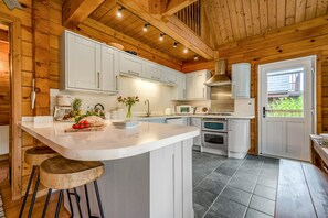 Una cocina con armarios blancos, una isla central con taburetes, una estufa y un microondas.