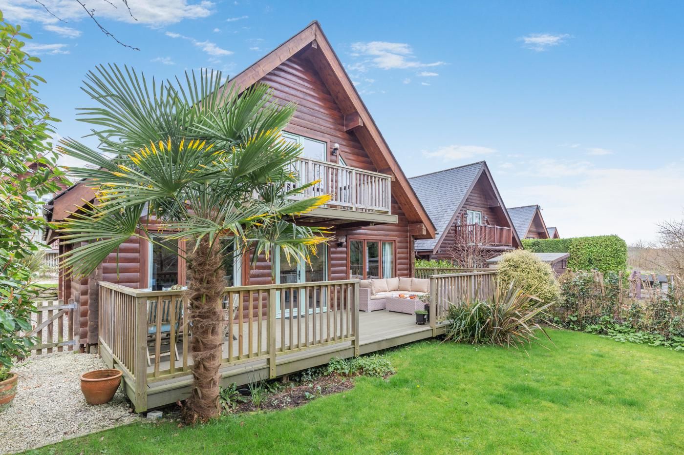 A wooden cabin with a balcony, a deck, and a well-maintained garden.