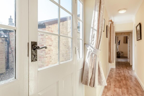 A hallway with a white door, a view of a brick building outside, and a wooden floor.