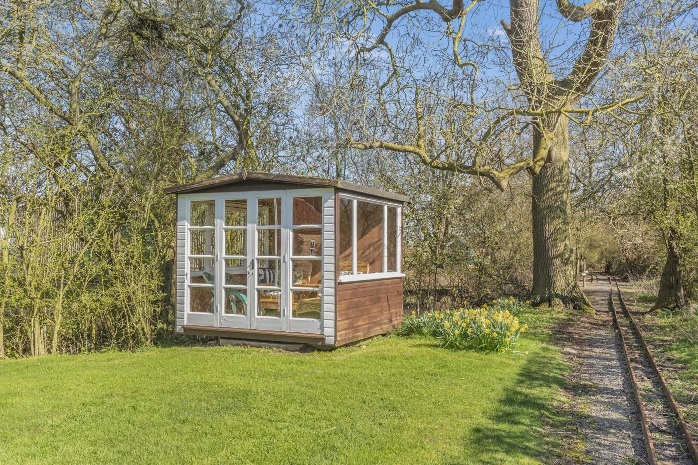A small wooden structure with large windows, surrounded by trees and a grassy area.