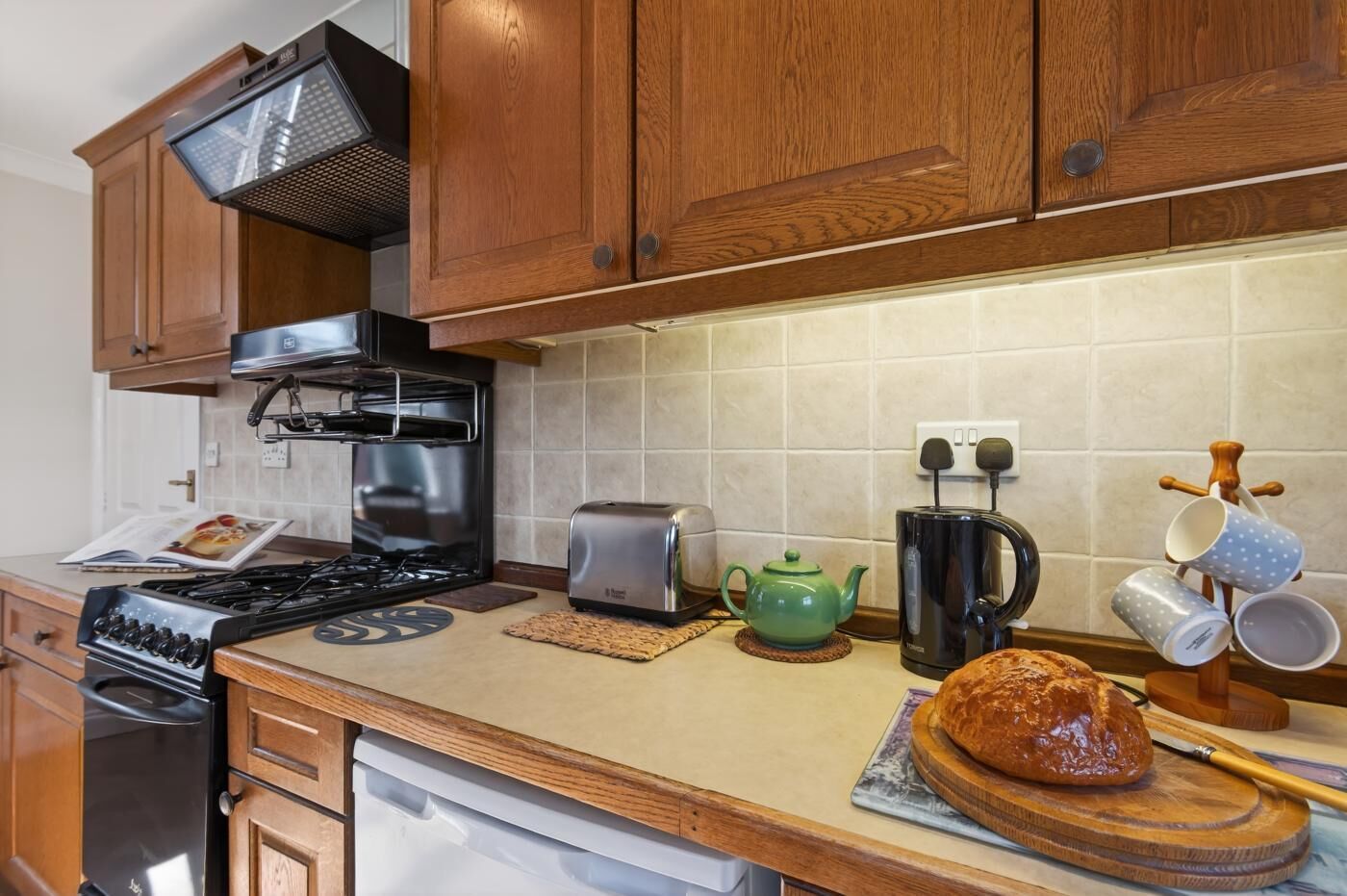 Una cocina con armarios de madera, estufa a gas, tostadora, hervidor y una barra de pan sobre la encimera.