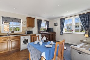 A kitchen with wooden cabinets, a washing machine, a dining table with chairs, and a sofa. - 1 Bed in Kirkby Green (oc-m34762) (Kirkby Green)