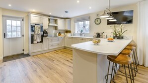 Een moderne keuken met witte kastjes, een centraal eiland, barstoelen, een groot raam en een flatscreen televisie boven het eiland.
