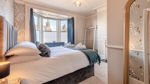 Una camera da letto con un letto grande, una finestra con tende, uno specchio decorato con motivi floreali e un lampadario.