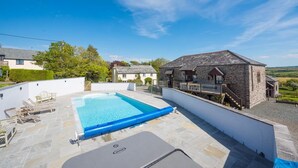 En swimmingpool med en terrass av sten, en byggnad i sten med en trappa och utsikt över landskapet.