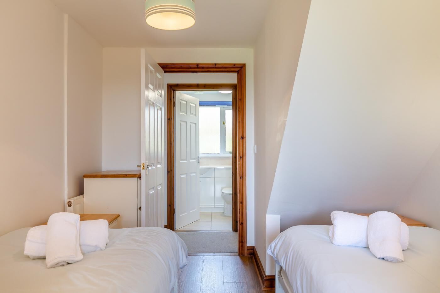 A room with two beds, a wooden door, and a view of a bathroom.
