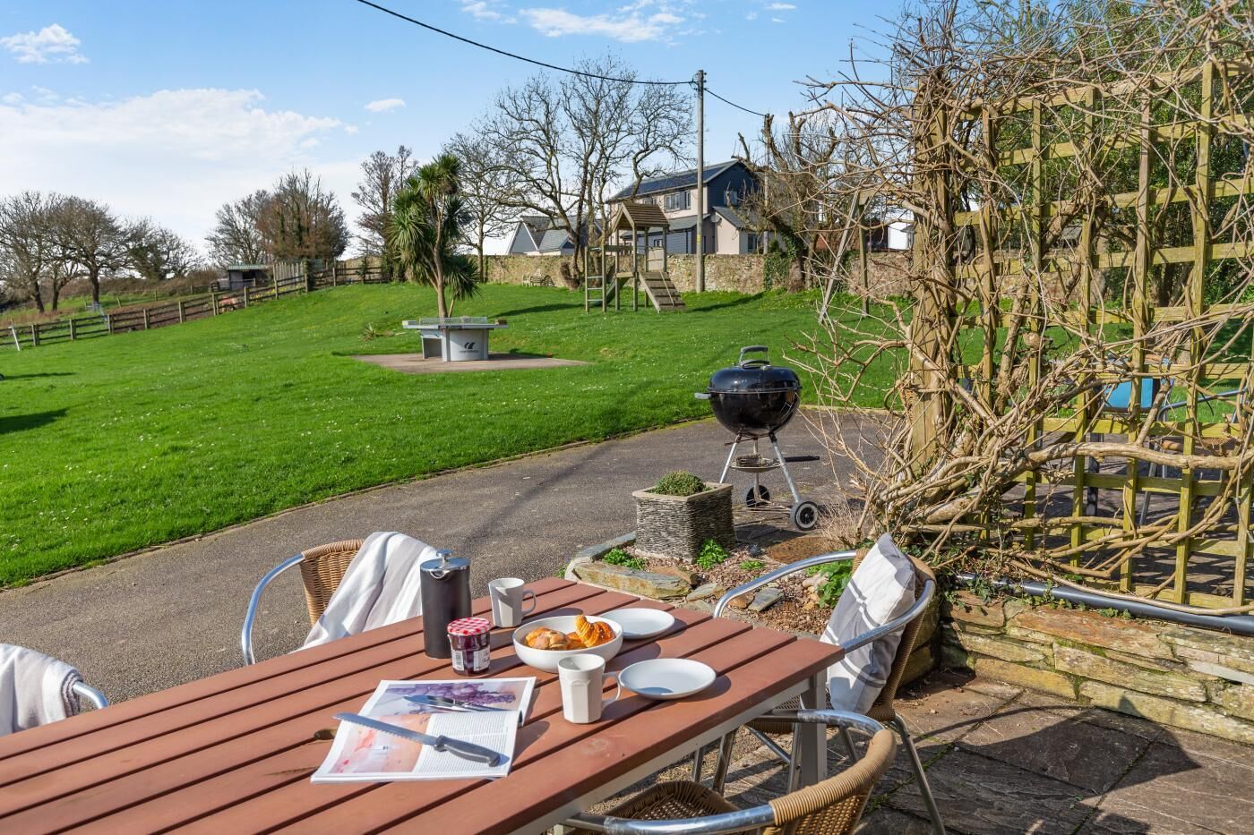Een buitenplaats met een houten tafel, stoelen en een barbecue.