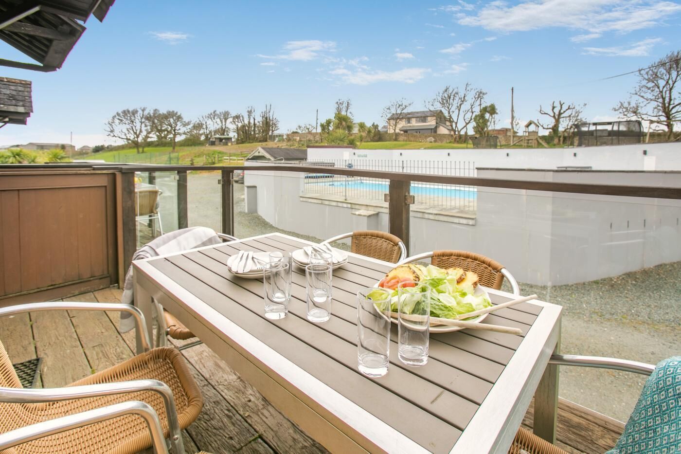 Eine Holzterrasse mit einem Tisch für zwei Personen mit Blick auf einen Swimmingpool.
