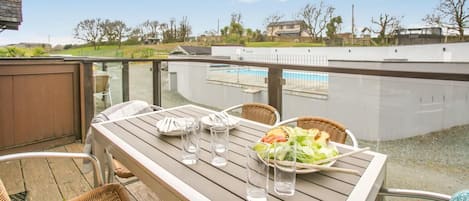 A wooden deck with a table set for two, overlooking a swimming pool.