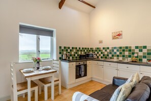 A compact kitchen with a dining area, a window with a view, and a sofa. - 1 Bed in Marhamchurch (oc-p34748) (Marhamchurch)