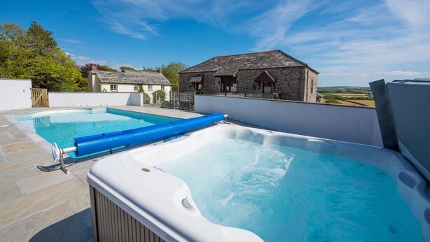 Un espace piscine sur le toit, comprenant un jacuzzi et une piscine plus petite, le tout entouré de bâtiments en pierre et surplombant un ciel dégagé.