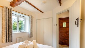 Une chambre à coucher avec un lit, une fenêtre avec des rideaux, un radiateur et une porte en bois.
