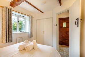 A bedroom with a bed, a window with curtains, a radiator, and a wooden door. - 1 Bed in Marhamchurch (oc-p34748) (Marhamchurch)
