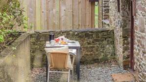 Un espace extérieur rustique aménagé avec une table, une chaise et un mur en pierre en arrière-plan.