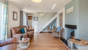 A spacious living area with a leather sofa, striped armchairs, a wooden coffee table, and a staircase leading to another level. - 4 Bed in Marhamchurch (oc-p34749) (Marhamchurch)