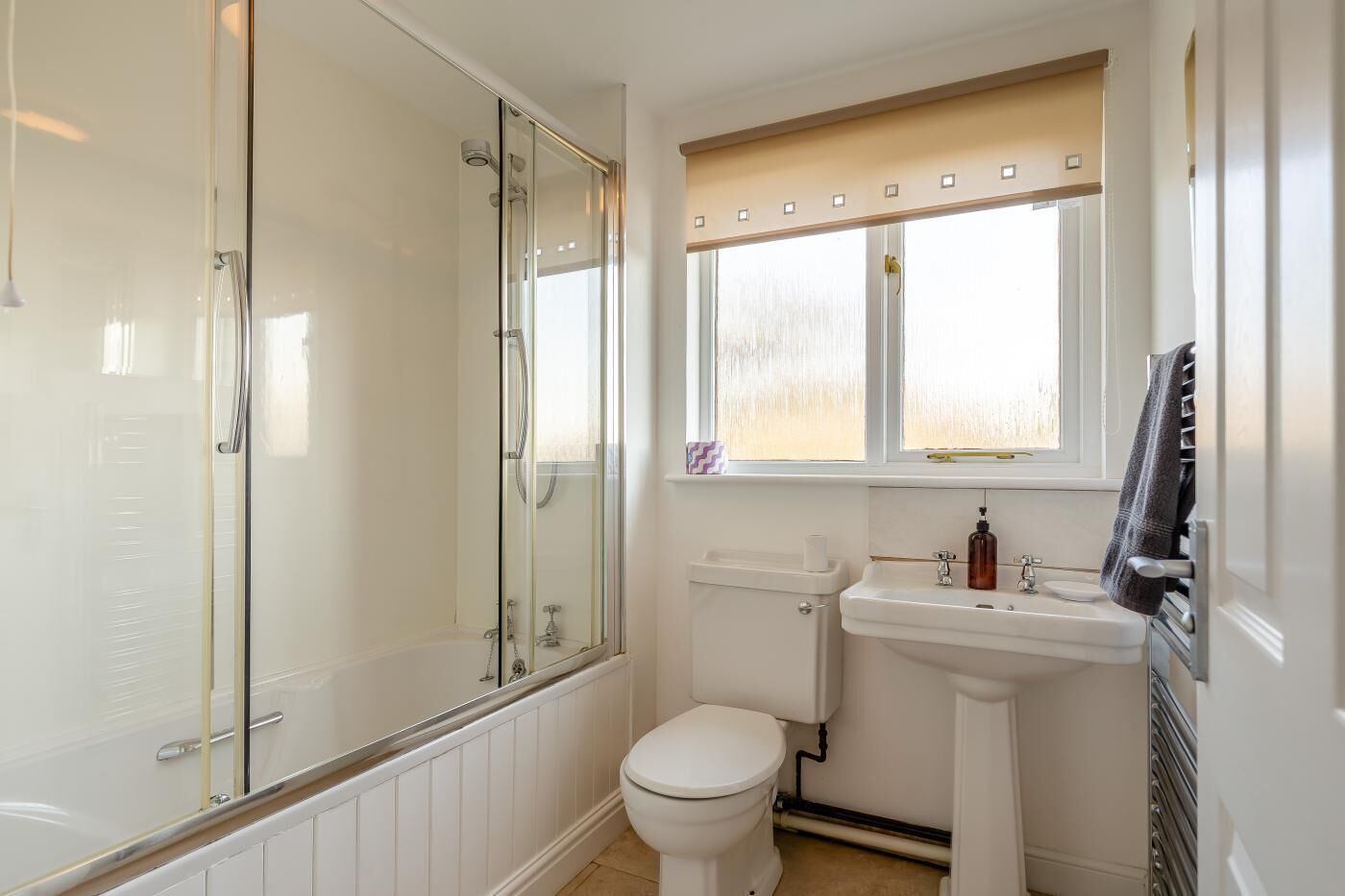 A bathroom with a glass-enclosed shower, a white toilet, a sink with a mirror, and a window above the sink.