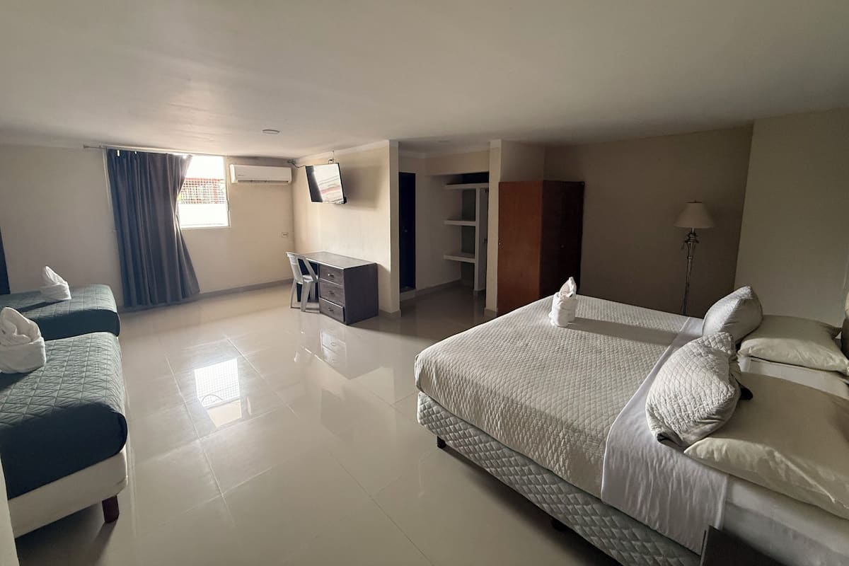Habitación de hotel con dos camas, un escritorio, una silla, un armario y un televisor.