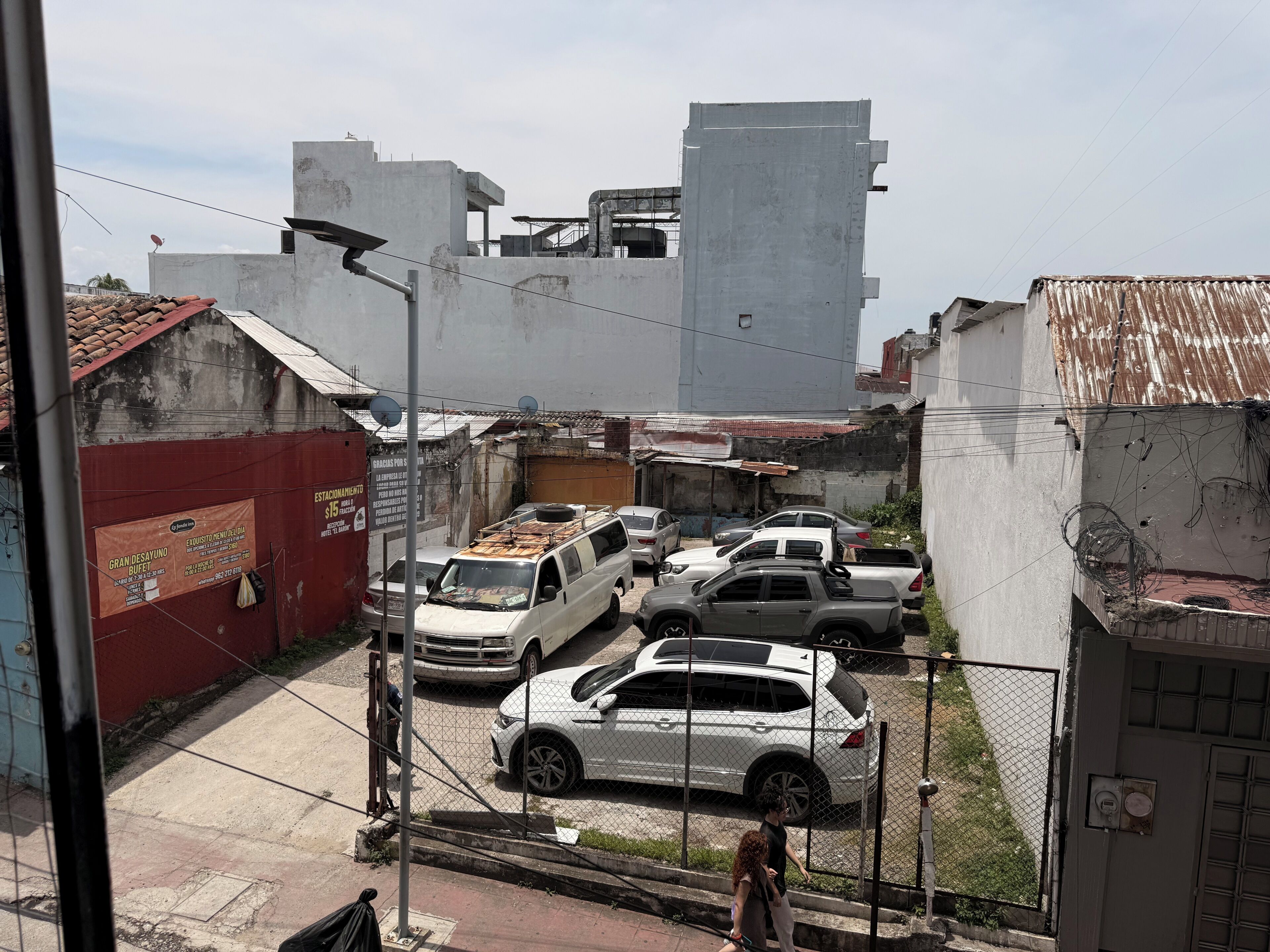 A parking area with several cars, a fenced area, and buildings with visible signage.